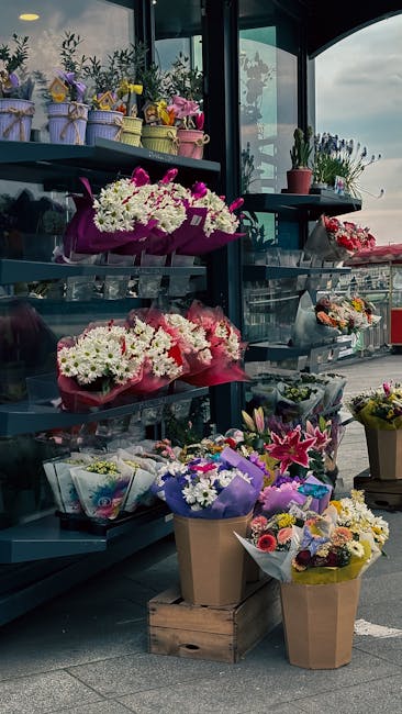 A display of various floral arrangements and bouquets outside a flower shop, featuring a range of fresh flowers including white daisies, pink lilies, and purple irises wrapped in colorful paper and ri
